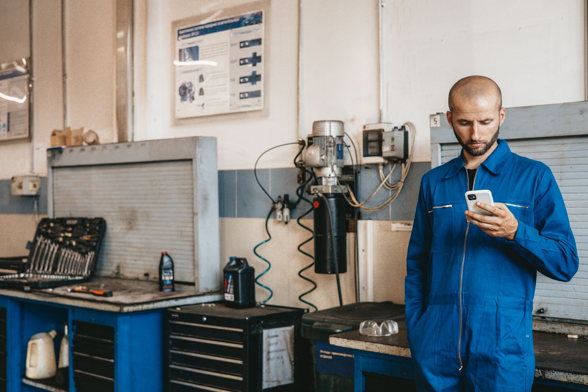 Handwerker schaut nachdenklich auf sein Smartphone in der Werkstatt